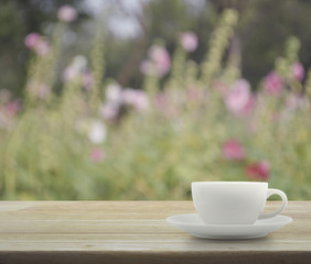 White cup on wooden table with blurred pink flower and tree, sof