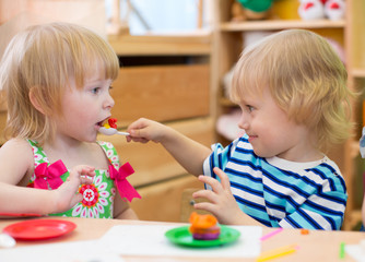 Two kids playing in kindergarten together. Boy feeding girl.