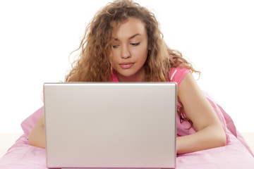 young beautiful woman lying on a bed, thinking and writing on a laptop