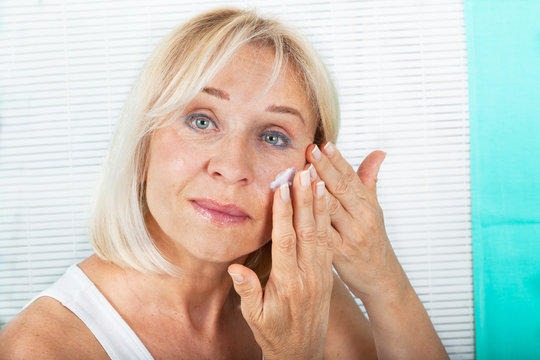 Woman in her 60s applying skin cream on her face. Anti-aging concept.