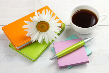 Notepad with pen and camomile on a white wooden background with Cup of strong coffee and stickers