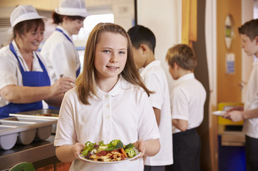 Girl holds a plate of food in school cafeteria, head turned