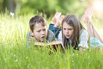 Mädchen und Junge lesen spannendes Buch auf der Wiese