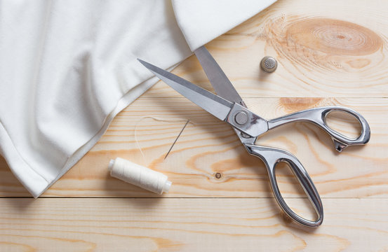 Cutting white fabric with a taylor scissors on wooden table