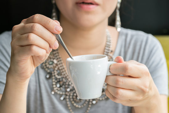 Hand of young woman stirring spoon in cup of coffee expresso
