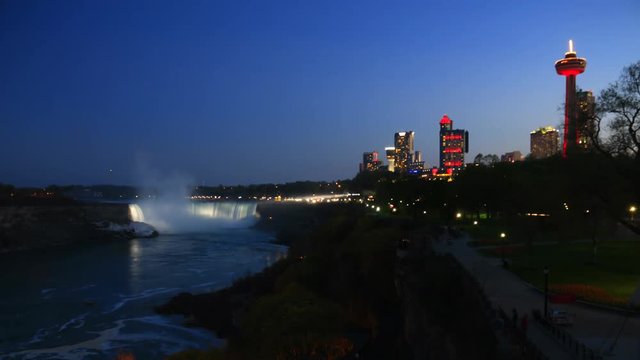 Niagara Falls City skyline 4k time lapse from dusk until night with colorful festival lights illuminating Horseshoe waterfalls and landmark buildings of hotels and casino. People walking cars driving