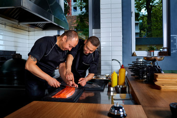 Two men cook chef cut up, cooked fish in restaurant commercial k