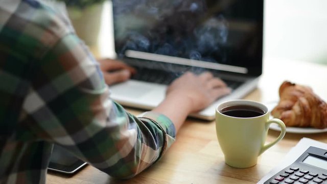 Cinemagraph of steaming coffee on desk of young programmer 