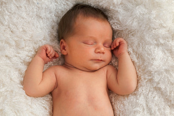 One week old baby sleeping on white blanket