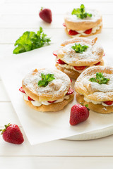 Homemade choux pastry rings with cottage cheese cream and strawberries decorated mint leaves on white wooden background