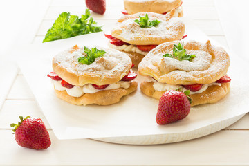 Homemade choux pastry rings with cottage cheese cream and strawberries decorated mint leaves on white wooden background