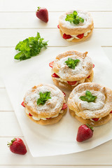 Homemade choux pastry rings with cottage cheese cream and strawberries decorated mint leaves on white wooden background