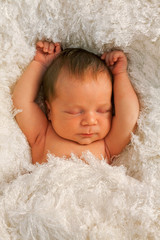 Cute week old baby sleeping on white blanket. Hands up. Vertical shot