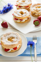 Homemade choux pastry rings with cottage cheese cream and strawberries decorated mint leaves on white wooden background