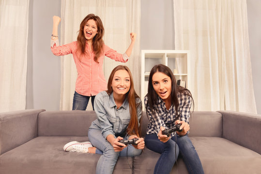 Excited happy girls sitting on sofa and playing video games