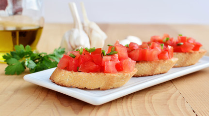 Tomato bruschettas on white platter over wooden table