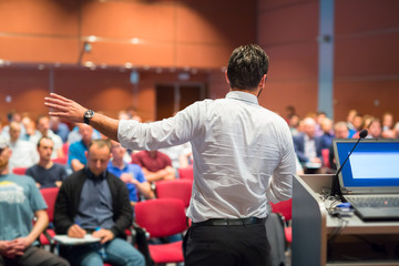 Speaker giving a talk on corporate Business Conference. Audience at the conference hall. Business...