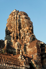 Fototapeta premium Dramatic view at sunset of one of the many large stone carved faces of Bayon Temple in Angkor Thom, Angkor district, Siem Reap, Cambodia