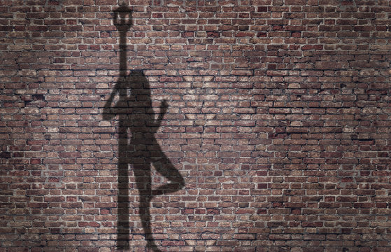 ombra di una prostituta appoggiata al lampione sul muro di mattoni 