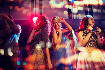 happy friends dancing in club with holidays lights