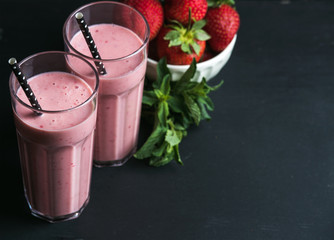 Strawberry and mint smoothie in tall glasses, bawl of fresh berries on dark rustic wood background