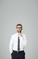 Young handsome businessman thinking on gray background.