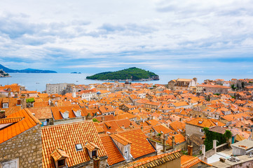 Fototapeta na wymiar Orange roofs of buildings in old town Dubrovnik and island Lokrum on background, Croatia