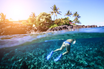 Young woman swimming on the bright coral reef in the sea on a background of a tropical beach
