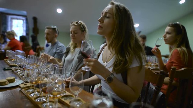 Group of young people on a wine tasting. Girl with a glass of wine, it tastes the drink taste and smell.