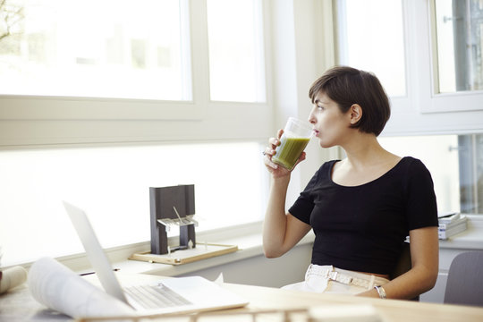 Portrait of woman drinking green smoothie in the office