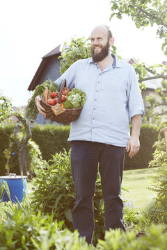 Young man standing in garden, basket with fresh vegetables