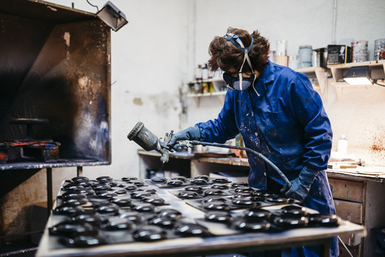 Female worker painting ceramics with spray gun