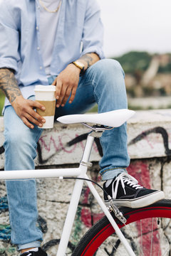 Young man with a bicycle and coffee to go sitting on graffiti wall