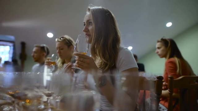 Group of young people on a wine tasting. Girl with a glass of wine, it tastes the drink taste and smell.