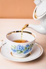 Old-style porcelain kettle pouring tea from jug to cup of tea