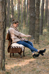 Hardworking, tired student work at the new project at laptop, computer in unusual atmosphere in forest outdoors. School girl do her homework at the computer and sit on the chair. Studens glances over.