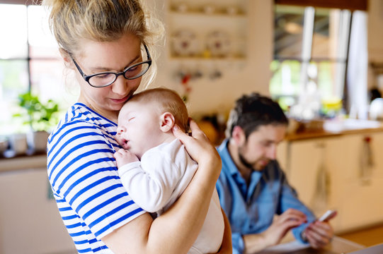 Mother holding little baby with father in background