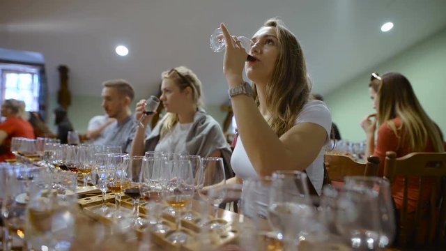 Group of young people on a wine tasting. Girl with a glass of wine, it tastes the drink taste and smell.