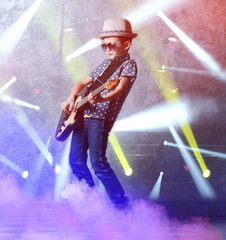 Little boy playing guitar on laser rays background