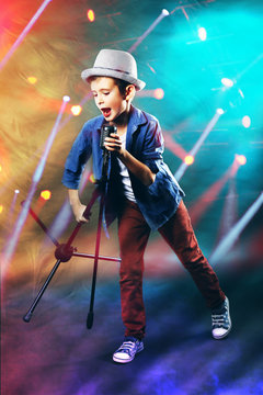 Little boy singing with microphone on laser rays background