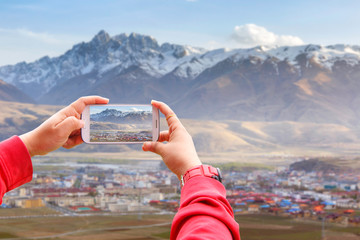 Smartphone photographing Village inclose mountain a famous landmark in Ganzi, Sichuan, China.
