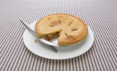 A sugar free apple pie with one slice cut out on a white plate atop a blue striped tablecloth