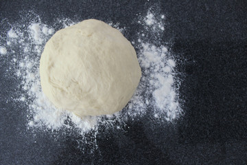 Ball of dough on a dark background with dusting of flour