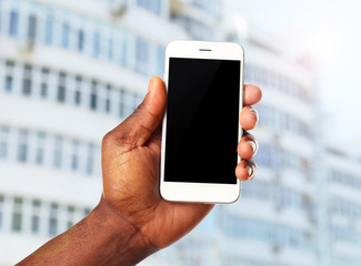 Hand shows mobile smart phone, urban city blurred background