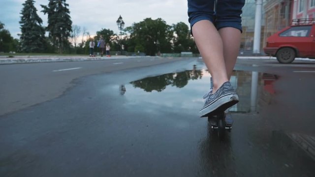 Young woman riding kick scooter in park in puddle, slow motion, close up shot