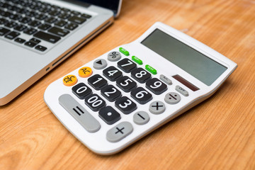 Calculator with laptop on wooden background