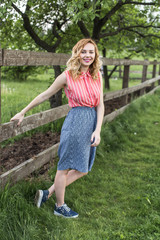 young happy girl standing at wooden fence in countryside