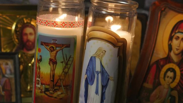 Religious candle burning with icones of jesus and mother Mary in the background. Filmed in 4K.