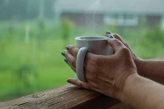 Female hands holding cup of coffee in the rainy day
