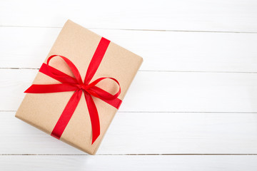 Gift box with red ribbon bow on white wooden background